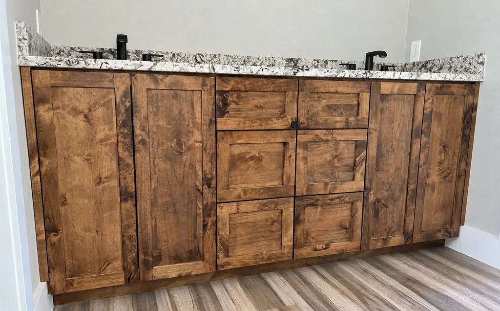 Knotty alder double vanity with shaker doors, center drawers, a granite top and two black faucets