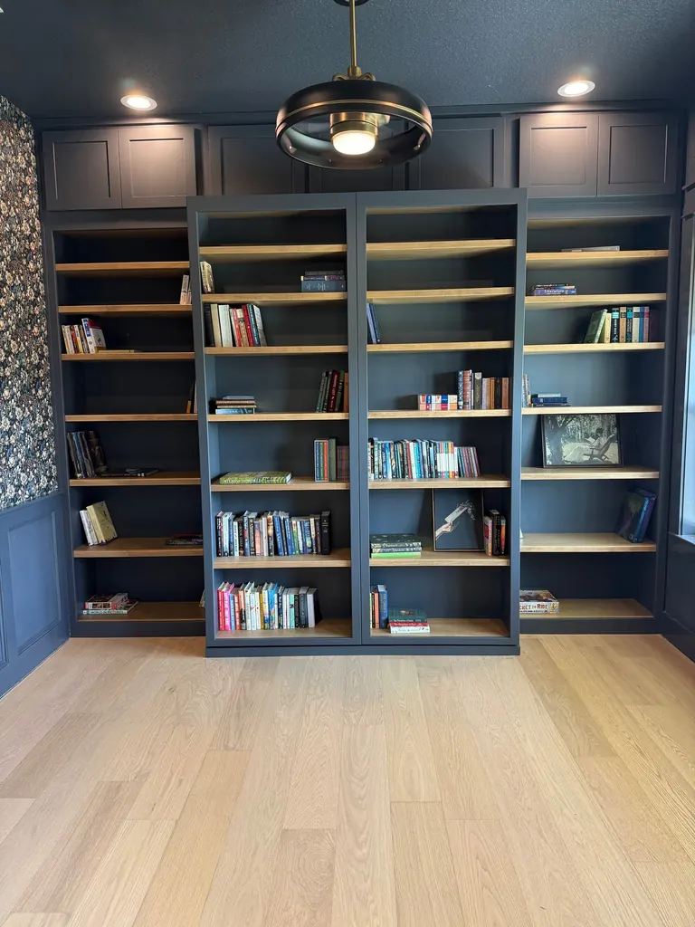 Navy built-in library wall with sliding bookcases, stained shelves and shaker upper cabinets