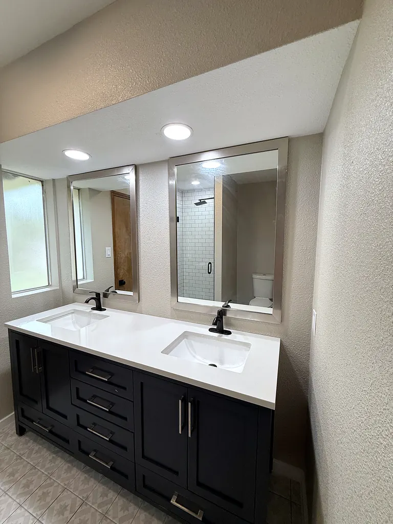 Double vanity with white quartz top, black faucets and framed mirrors; subway-tile glass shower visible in mirror