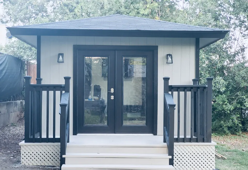 Finished backyard studio with black French doors, wall sconces, a front porch with railings and lattice skirting