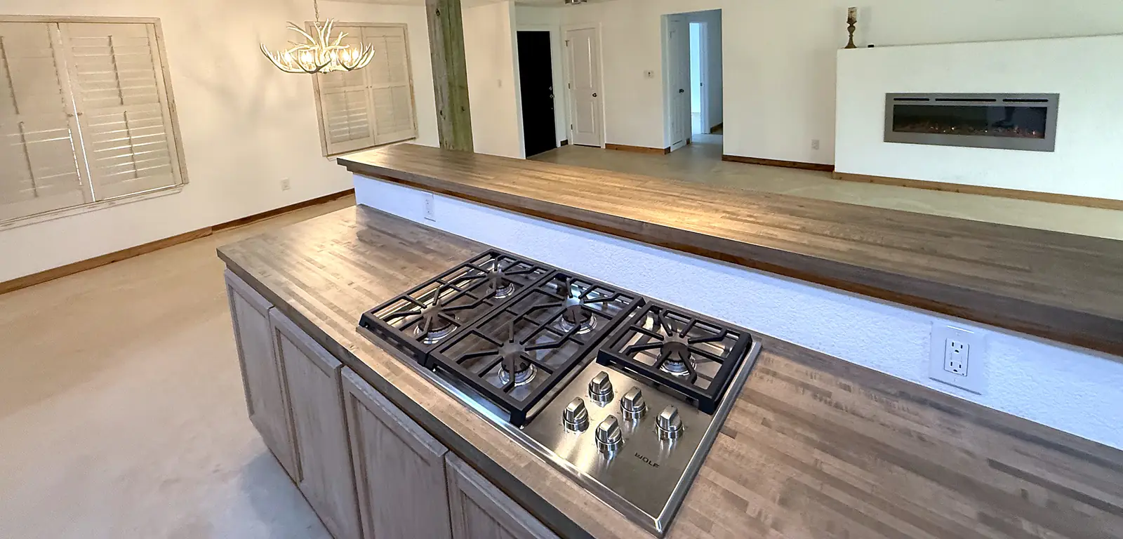 Island with butcher-block top, gas cooktop and stainless island hood, open living area behind