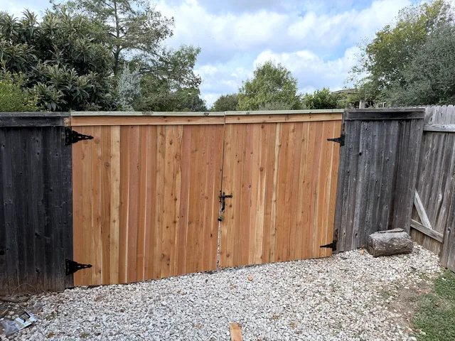 New cedar double drive gate with black strap hinges set between weathered fence sections