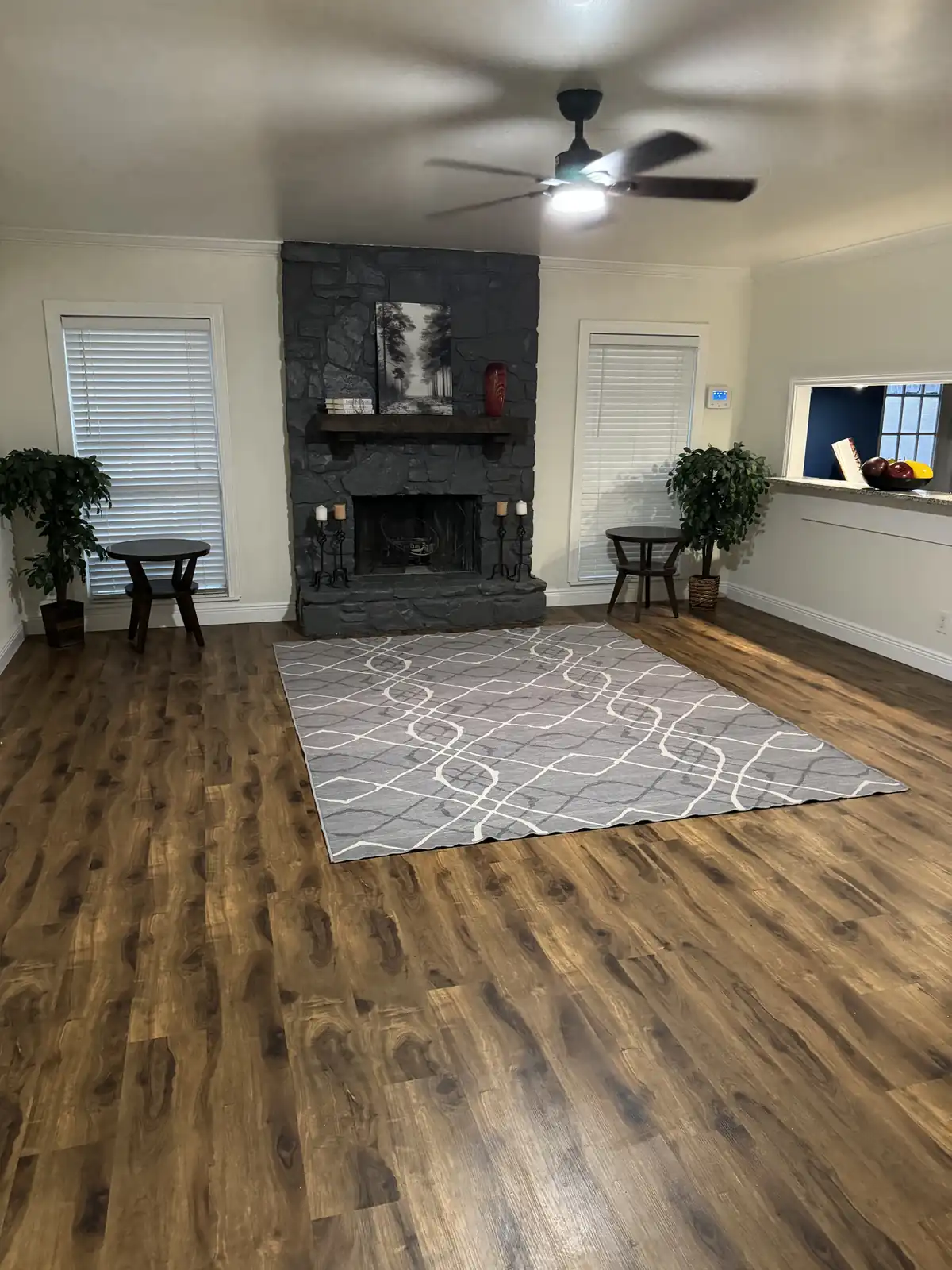 Living room with a painted charcoal stone fireplace, fresh light walls and new wood-look plank floors