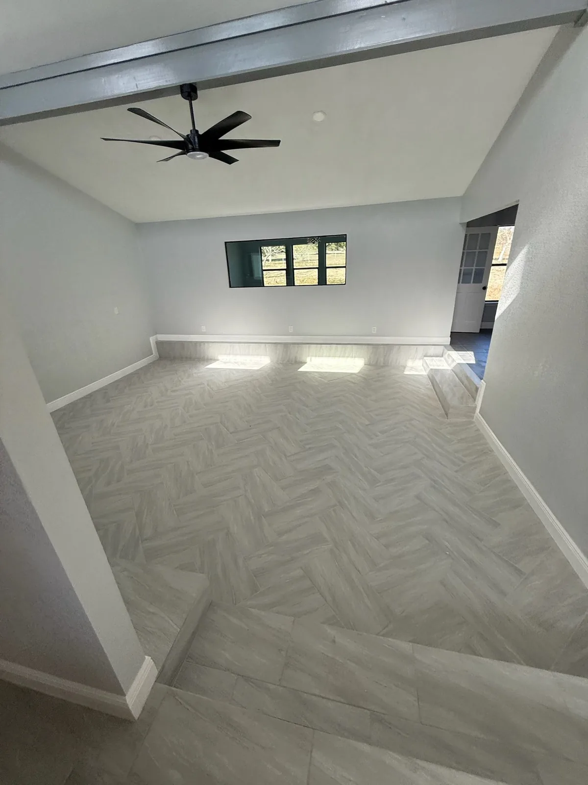 Bright room with a herringbone plank tile floor, a painted beam, a step-down and a ceiling fan