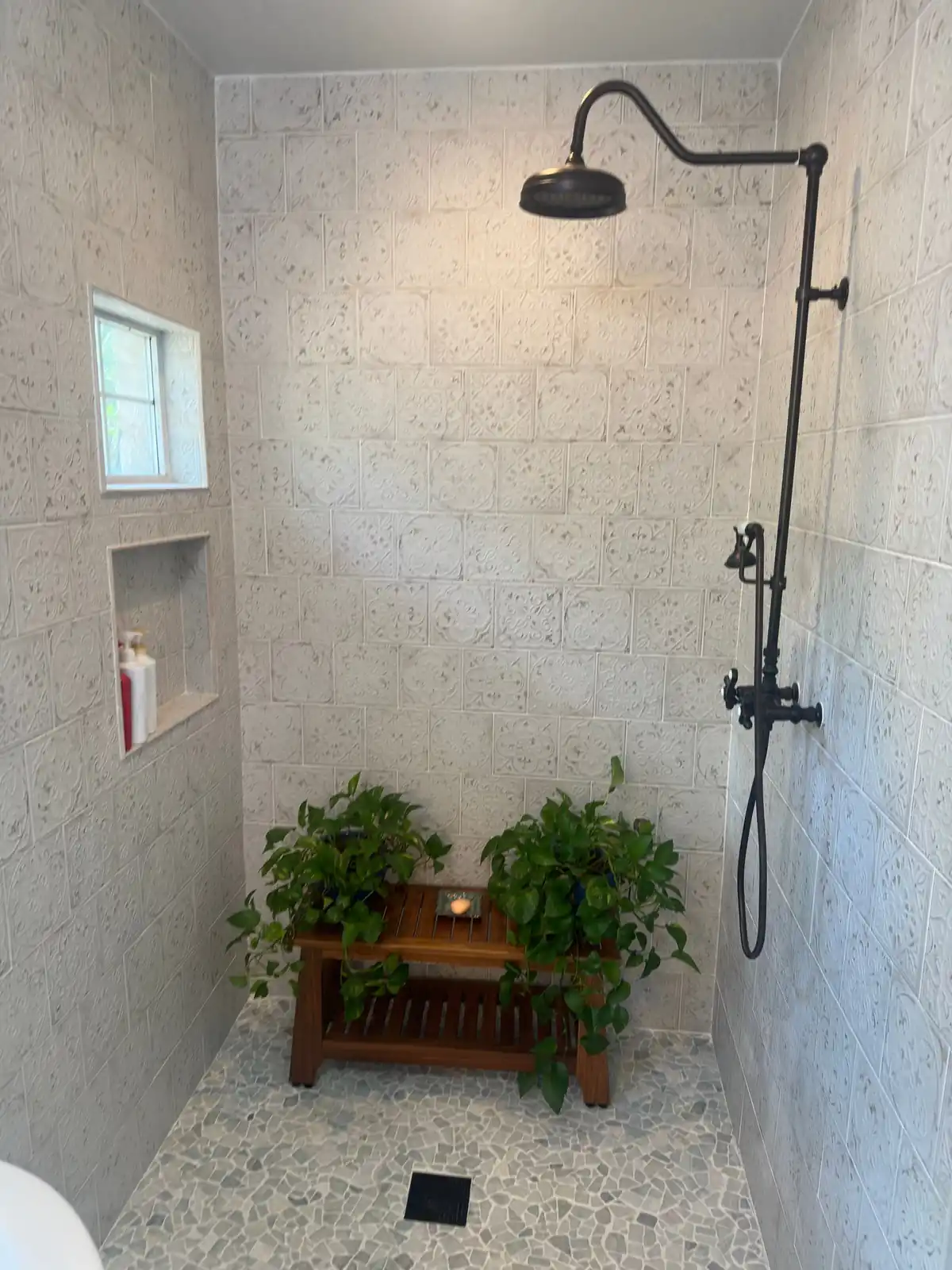 Open shower with stone-look wall tile, a recessed niche and an exposed black rain shower riser