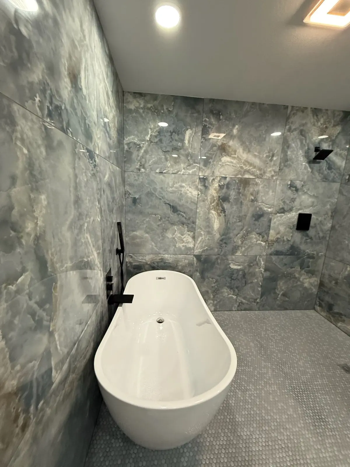 Wet room with large blue-grey marble-look tile, a penny-round floor and a freestanding tub